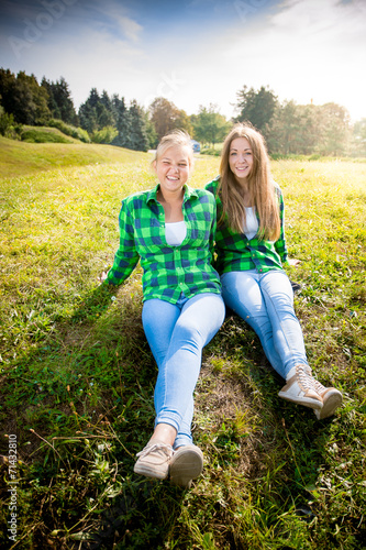 Two smiling hipster girls sitting on grass hill