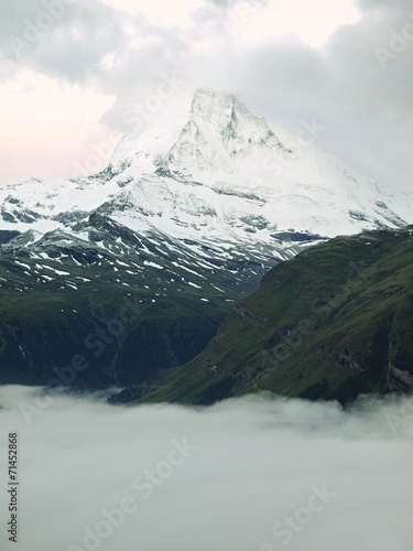Misty sharp peaks of Alps mountains above heavy fog in valley.