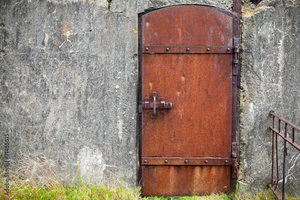 Rusted metal door in old fortification wall, background texture