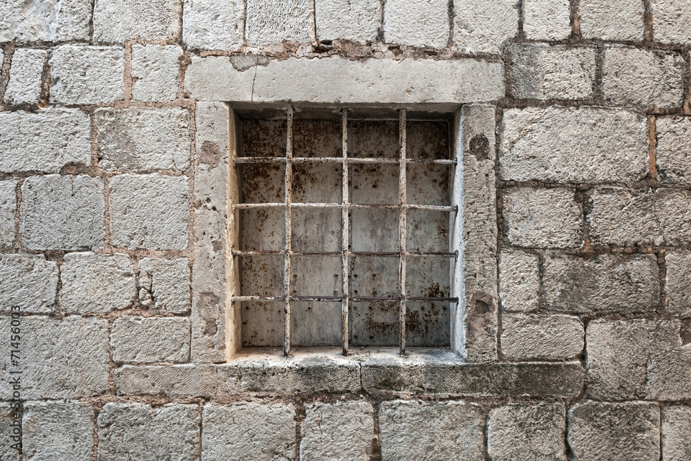 Locked ancient stone prison wall with metal window bars