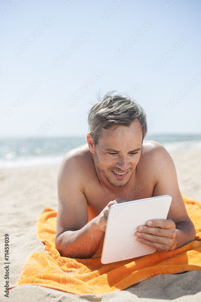 handsome man on the seaside lying on a beach towel to use a digi