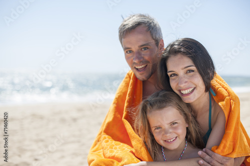 family of three people at the seaside sheltering under a beach t