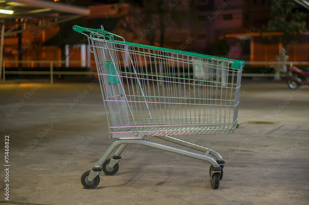 Empty shopping cart with green handle on parking near supermarke Empty shopping cart with green handle on parking near supermarke