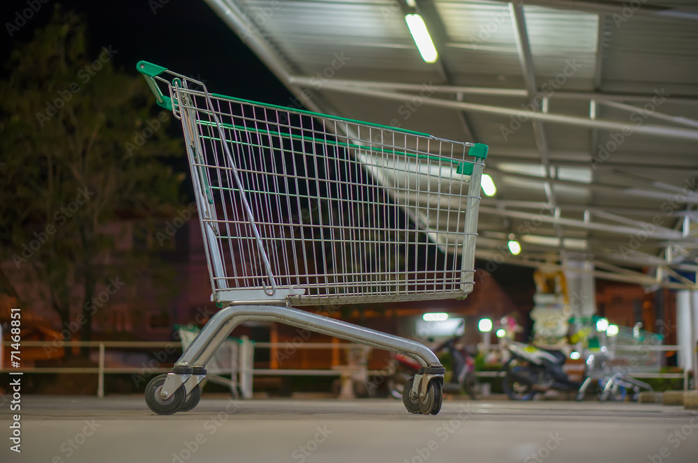 Empty shopping cart with green handle on parking near supermarke Empty shopping cart with green handle on parking near supermarke