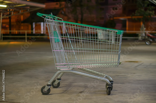 Empty shopping cart with green handle on parking near supermarke