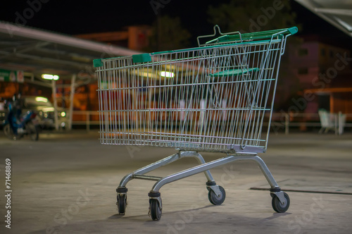 Empty shopping cart with green handle on parking near supermarke
