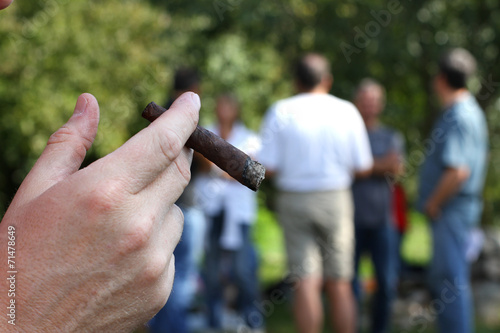 hand with cigar and many people in the background out of focus