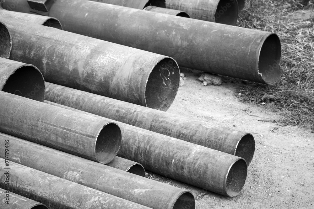 Rusted industrial steel pipes lay on ground, monochrome photo