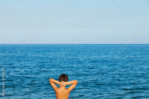 Child at sea. Child with arms behind his head looks at the horizon in front of him. The sea and the infinite make him think
