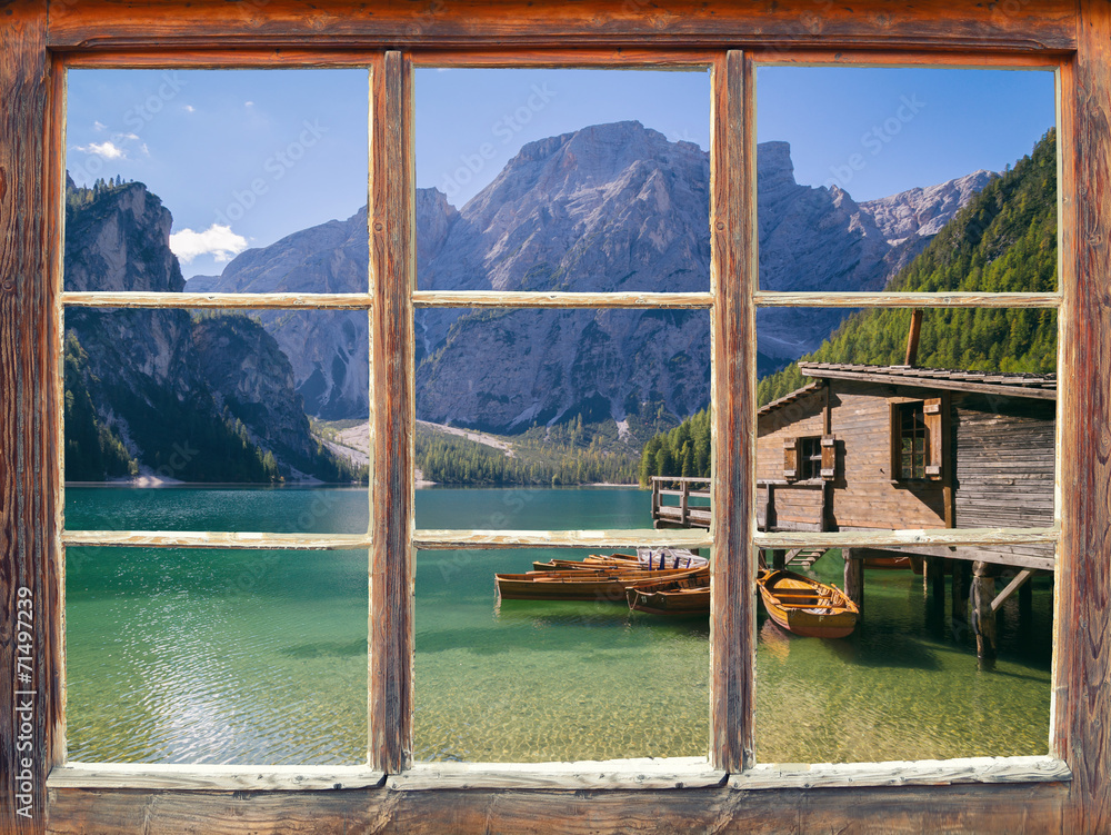Fototapeta Piękny widok z zamkniętego okna na góry,  pływające łódki na wodzie i drewniany domek