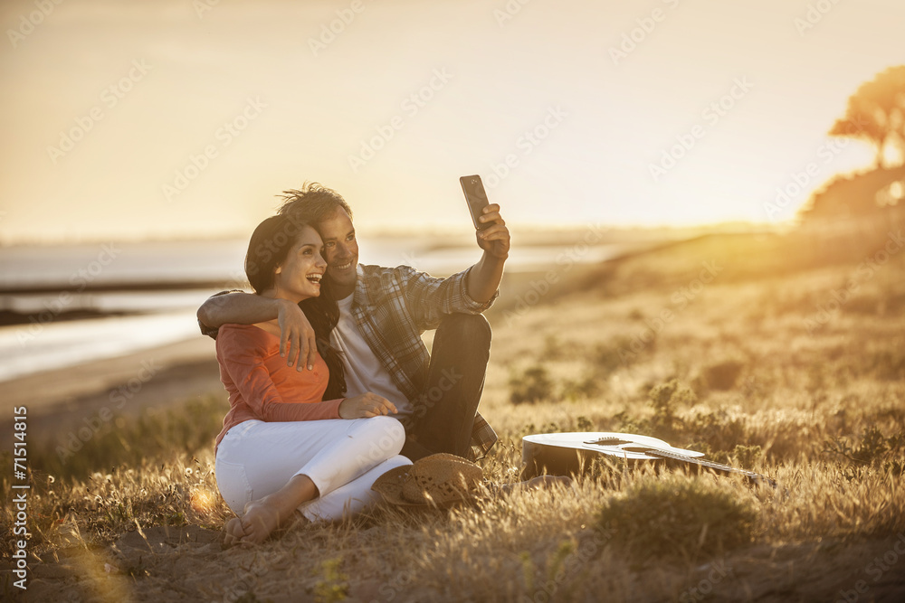 Romantic couple sitting on the beach at sunset and taking a self