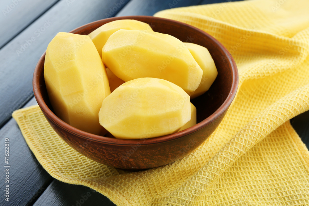 Raw peeled potatoes in bowl  on color wooden background