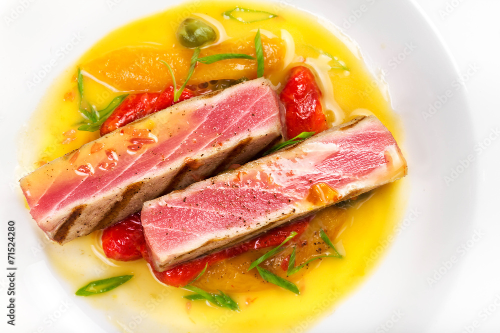 Grilled tuna steak with sauce, herbs and cherry tomatoes in a wh