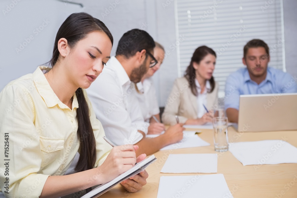 Woman taking notes while colleagues are talking behind her Woman taking notes while colleagues are talking behind her