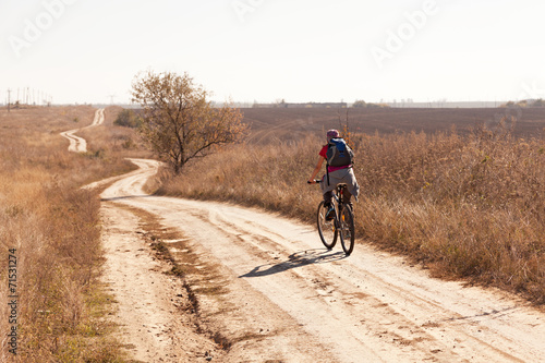 Woman riding a mountain bike on a rural  road, back view.