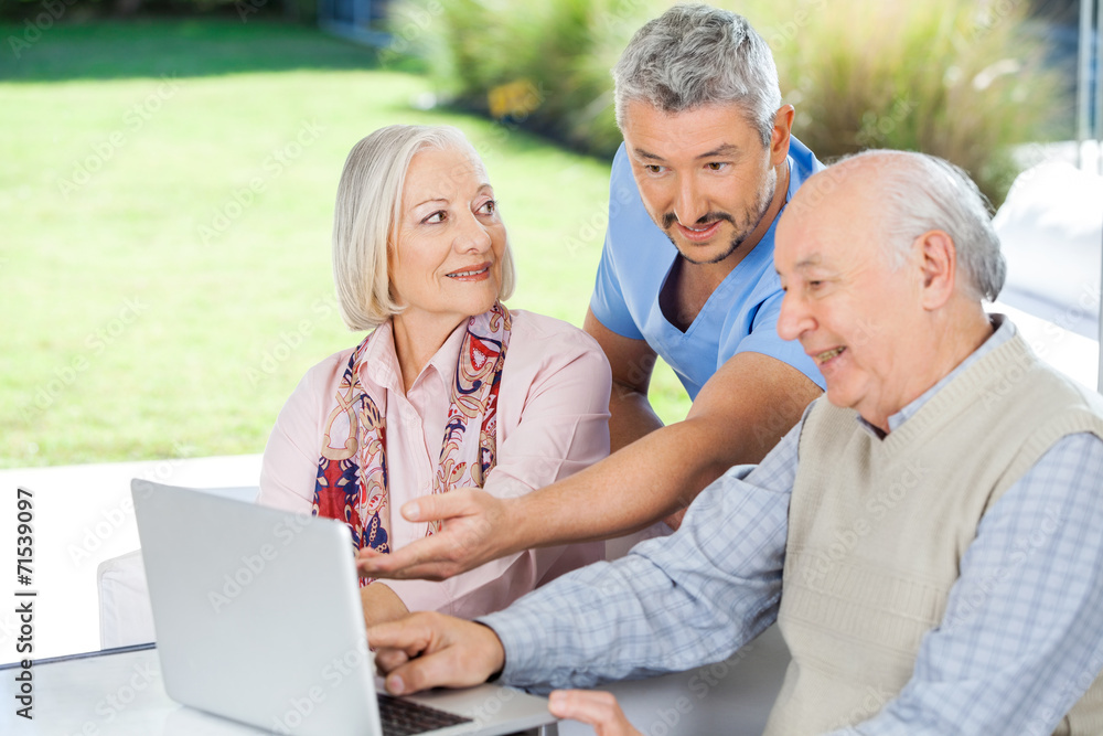 Male Caretaker Showing Something To Senior Couple On Laptop Male Caretaker Showing Something To Senior Couple On Laptop
