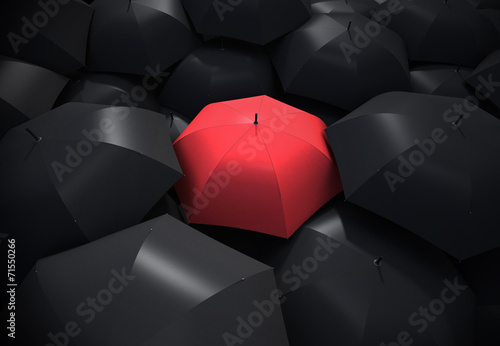 Red umbrella standing out from background of black umbrellas