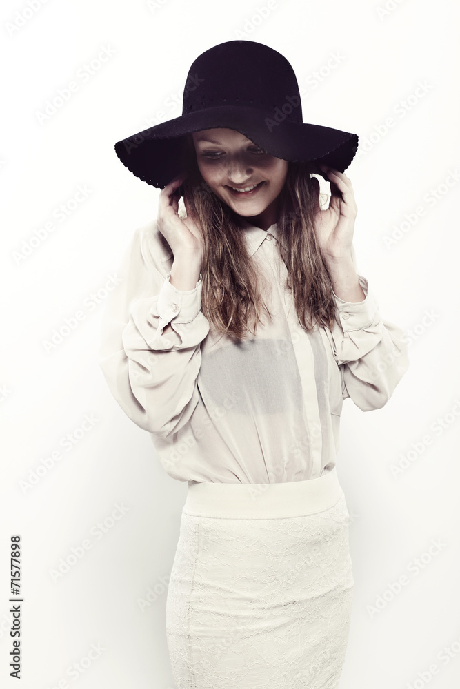 Young woman in black hat looking down in studio, smiling Young woman in black hat looking down in studio, smiling