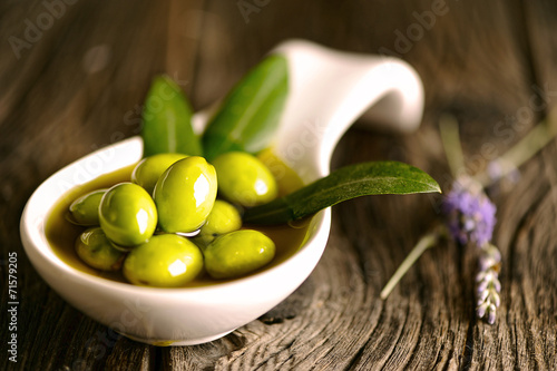 Green olives in the bowl and olive branch on wooden table