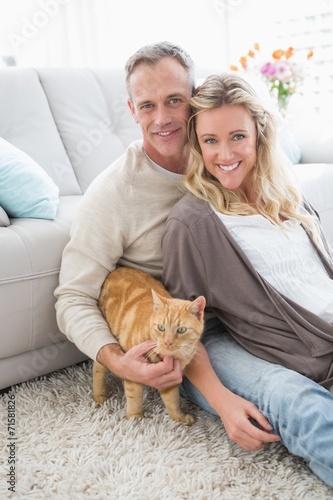 Smiling couple petting their gringer cat on rug photo