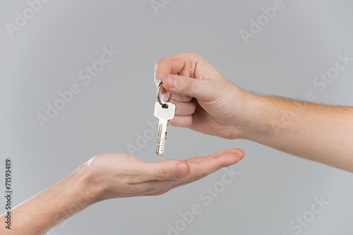 Male hand holding key and handing it over to another person.