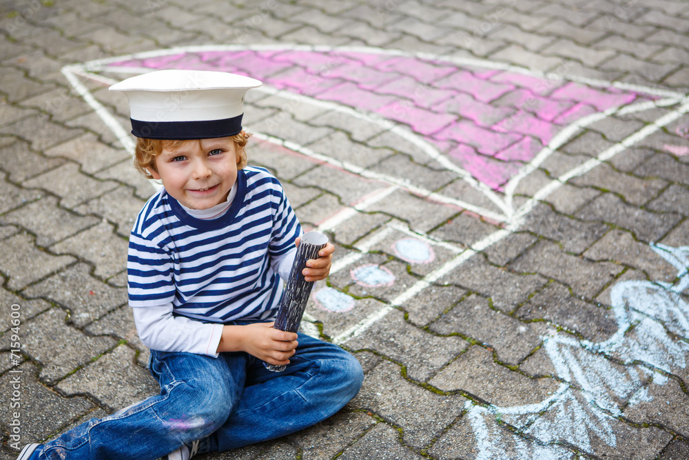 Little kid boy having fun with ship picture drawing with chalk