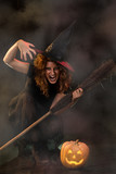 Woman dressed like a witch. She is with broom and pumpkin.