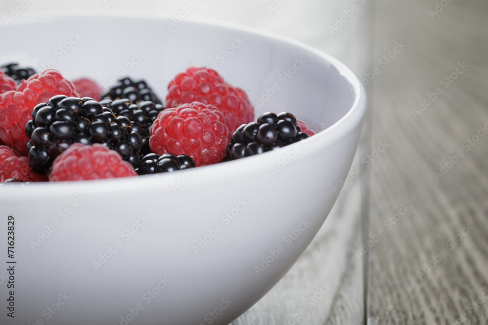 ripe blackberries and raspberries in white bowl on old oak table ripe blackberries and raspberries in white bowl on old oak table