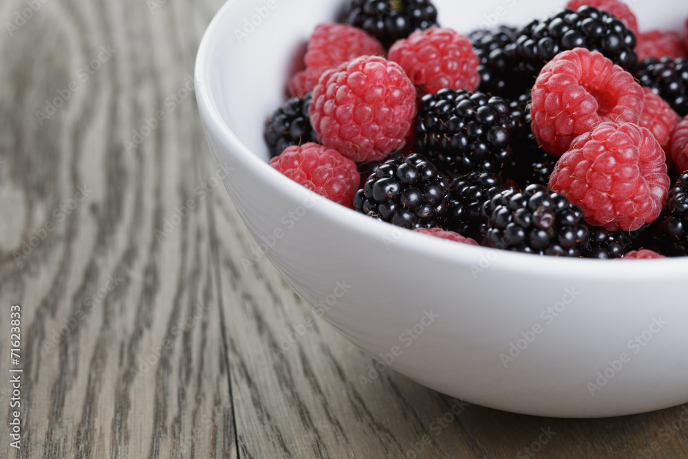 ripe blackberries and raspberries in white bowl on old oak table ripe blackberries and raspberries in white bowl on old oak table