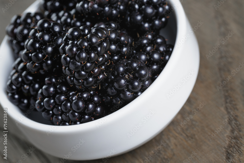 ripe blackberries in white bowl on old oak table