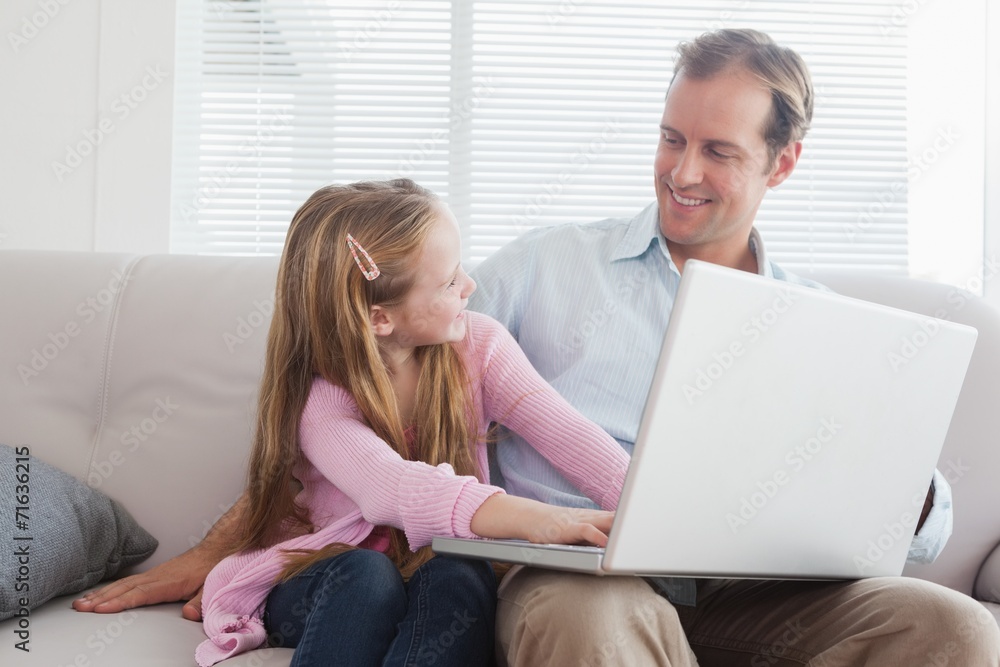 Casual father and daughter using laptop on the couch