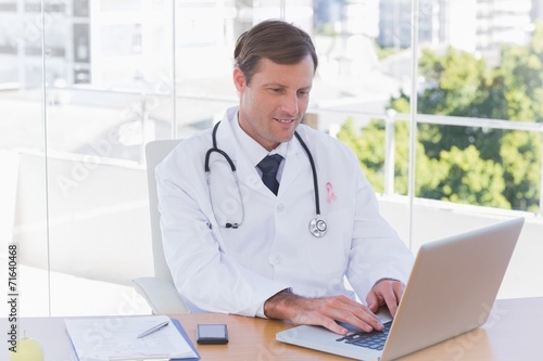 Composite image of happy doctor working on a laptop