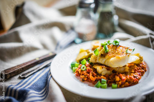 Roasted hake with romesco sauce and onion on wooden background