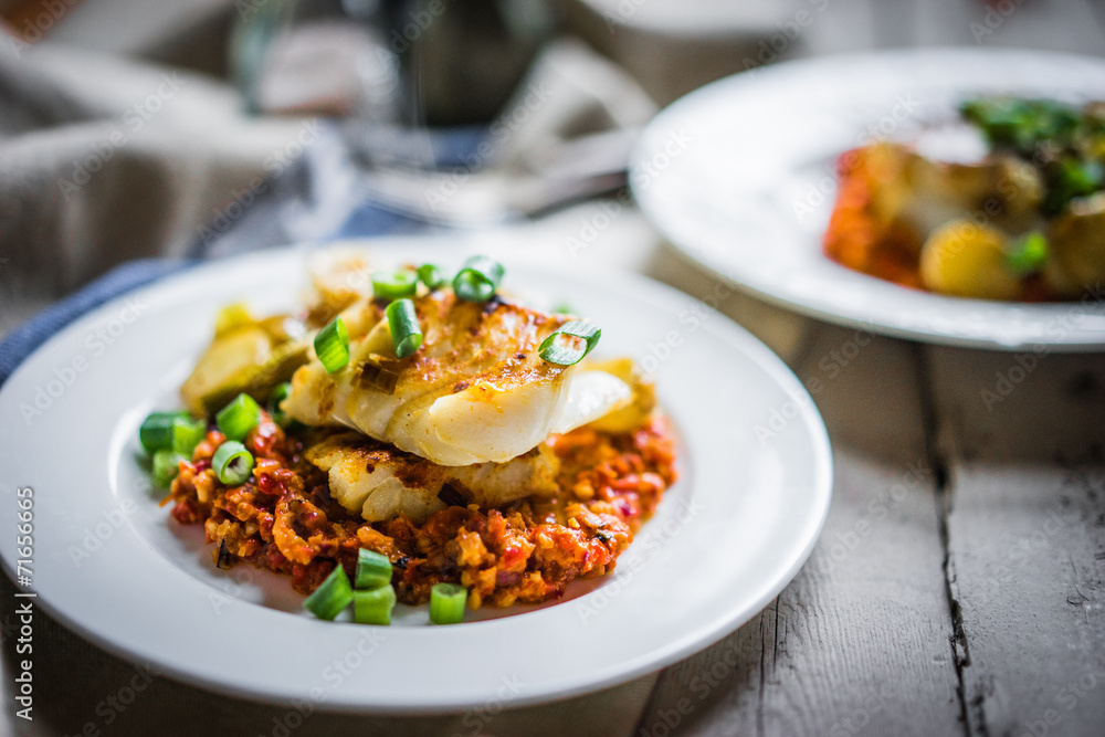 Roasted hake with romesco sauce and onion on wooden background Roasted hake with romesco sauce and onion on wooden background