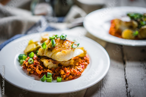 Roasted hake with romesco sauce and onion on wooden background photo