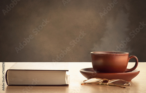 Book, glasses and cup of hot tea on a dark brown background