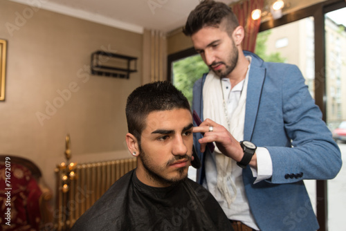 Male Hairdresser Cutting Hair Of Smiling Man Client
