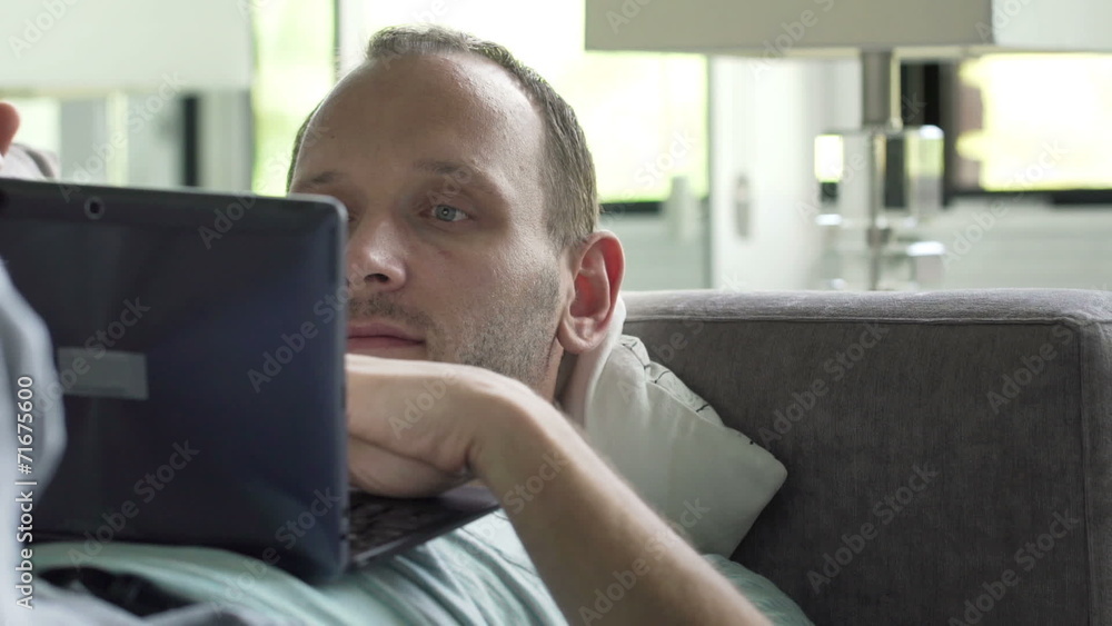 Young man with laptop lying on sofa at home Young man with laptop lying on sofa at home