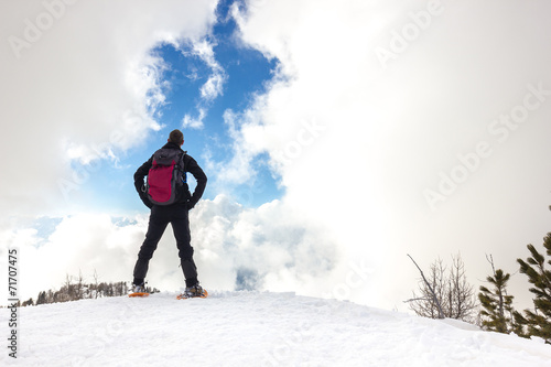 Uomo osserva cielo con nuvole in montagna d'inverno con ciaspole