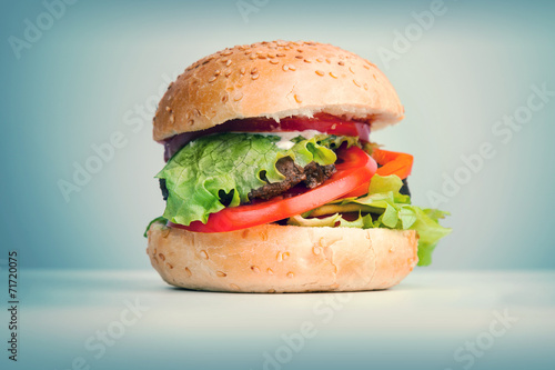 Big hamburger lays on the table above blue background, retro ton
