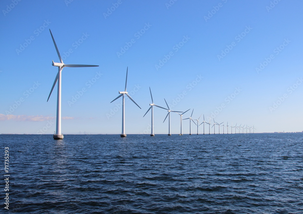 Perspective line of ocean wind mills with dark water and sky