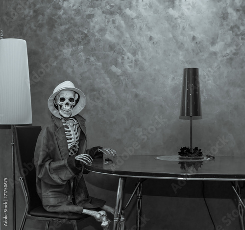 Skeleton sitting behind the table in dark dramatic room photo