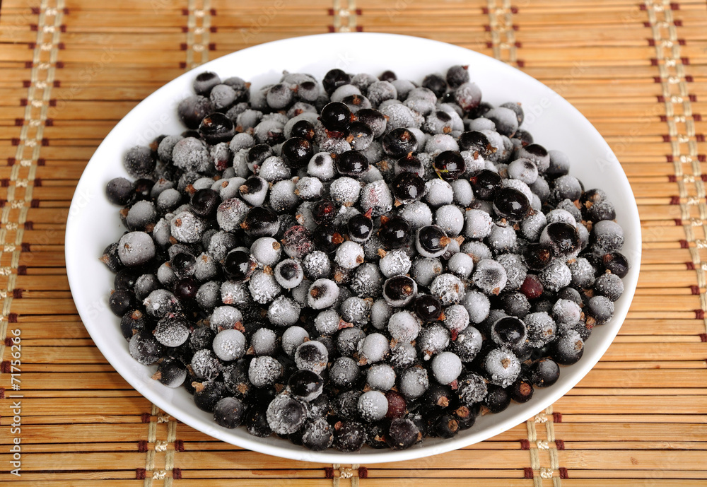 heap of frozen black currant in a plate on the bamboo cloth heap of frozen black currant in a plate on the bamboo cloth