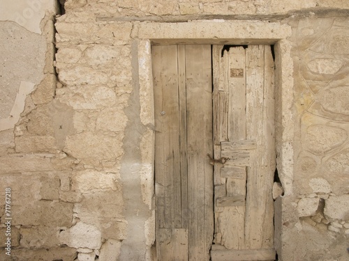 Bröckelndes Mauerwerk aus Naturstein und alte Holztür in Khaki un d Naturfarben in den Gassen der Altstadt von Alacati bei Cesme am Ägäischen Meer in der Provinz Izmir in der Türkei photo