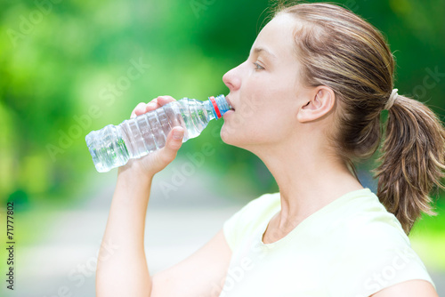 Woman drinking cold mineral water from a bottle after fitness ex