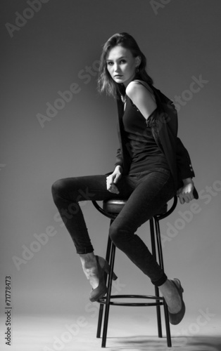 stylish adult girl in a jacket sits on a chair on a gray backgro