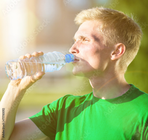 Tired man drinking water from a plastic bottle after fitness