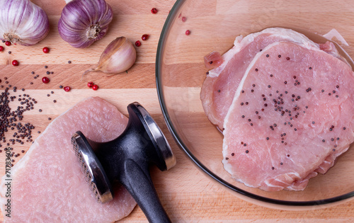 Raw pork schnitzel with meat tenderizer on wooden board photo