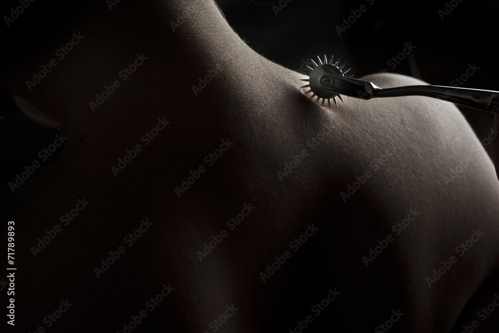 Fototapeta premium Nude submissive woman shoulder, bdsm act with Wartenberg wheel