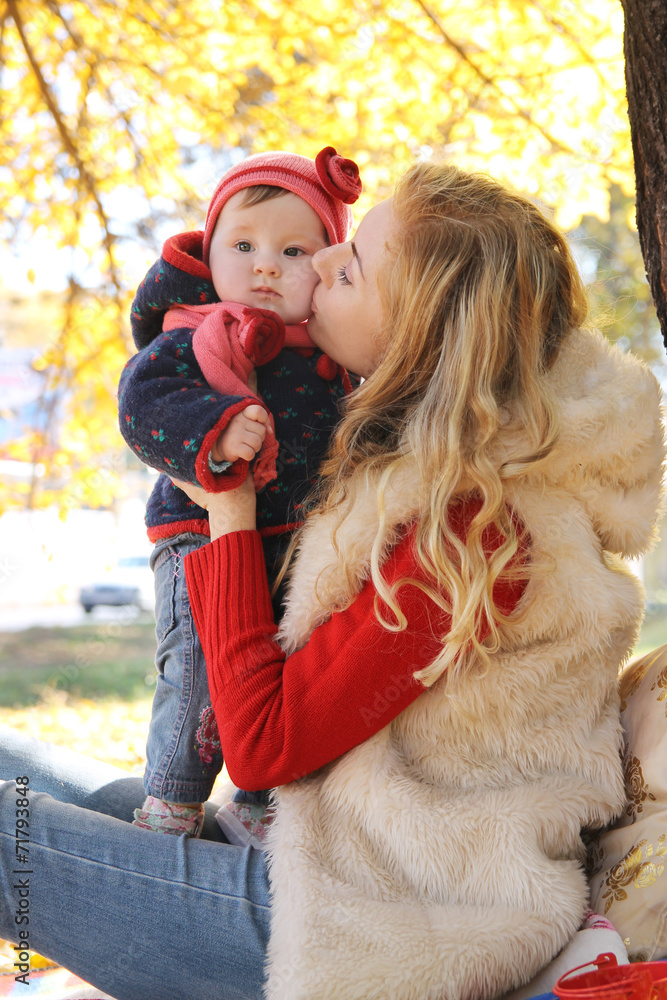 Mother kissing her baby girl under autumn tree Mother kissing her baby girl under autumn tree
